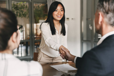 two employers sitting in office and shaking hand of young asian woman